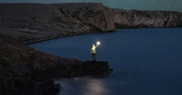 Traveller holding a lantern on a rocky shore at night